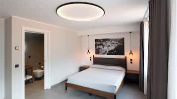 Een moderne slaapkamer met een bed, nachtkastjes, een hoofdbord, een wandlamp en een badkamer die door een geopende deur zichtbaar is.