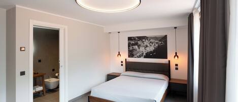 A modern bedroom with a bed, bedside tables, a headboard, a wall-mounted light fixture, and a bathroom visible through an open door.