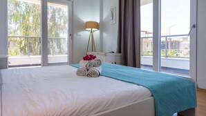 A hotel room with a large bed, a floor lamp, and a view of the outside. - EV Apartments (Serik)