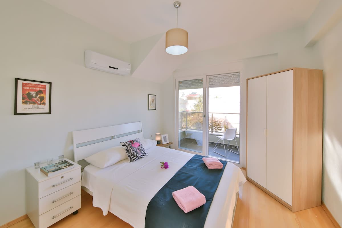 A bedroom with a bed, bedside table, wardrobe, and a window with a view of the outside.