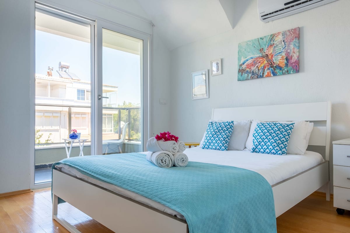 A bedroom with a bed, a window, and a painting on the wall.