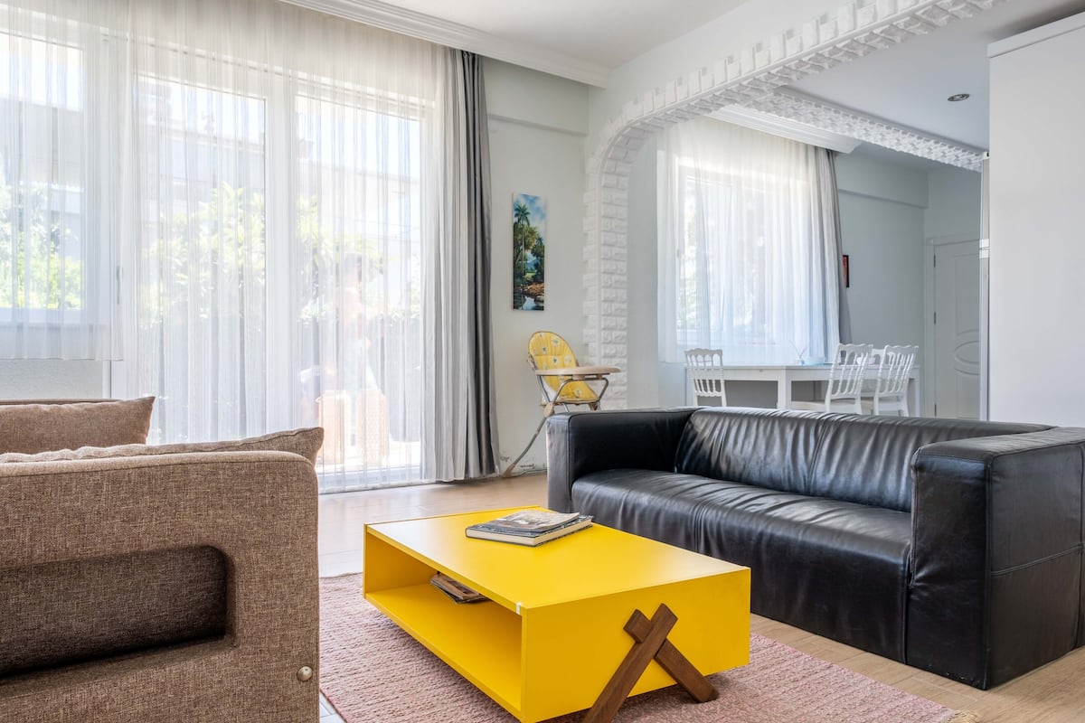 A modern living room with a black leather sofa, a yellow coffee table, and a brown armchair.