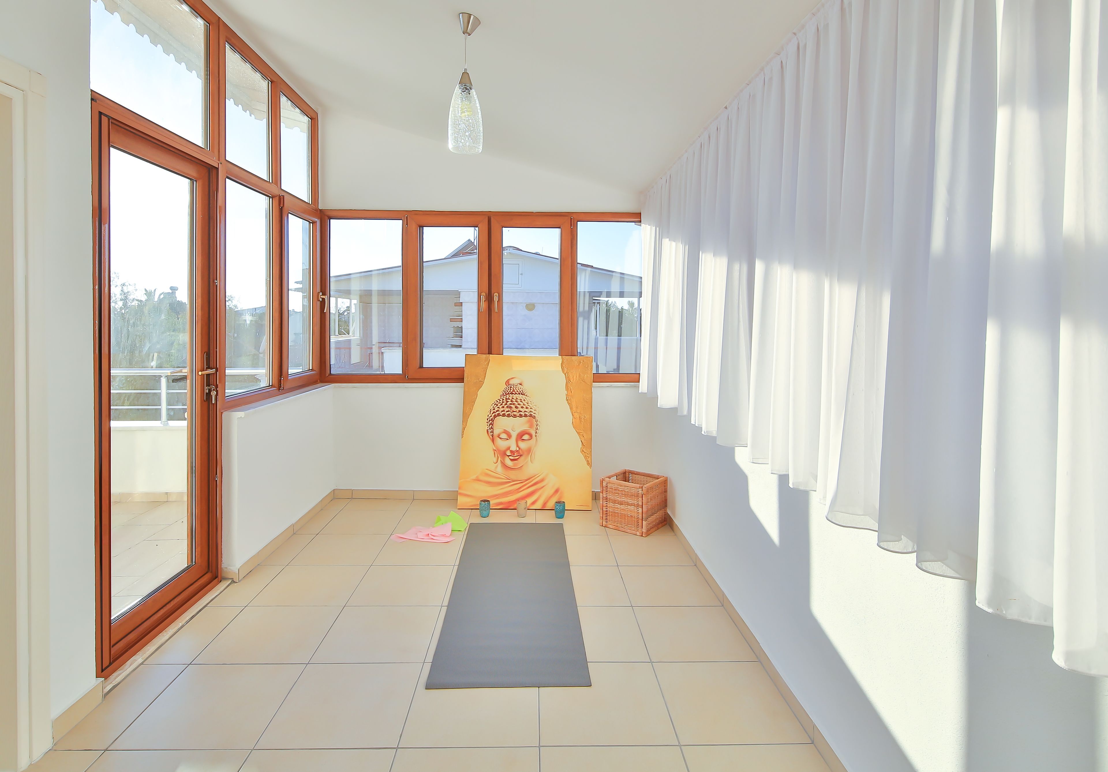 Una habitación con ventanas amplias, una colchoneta de yoga, un cuadro de Buda y una cesta de mimbre.