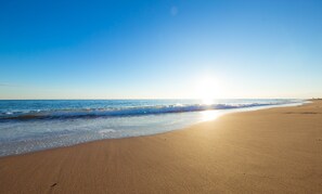 Una playa con cielo despejado y reflejos de sol sobre la arena.