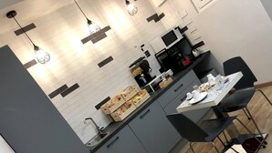 A modern kitchen with grey cabinets, a white tiled backsplash, and pendant lighting. There is a dining table set with plates, cups, and cutlery. - Avec Moi Roma (Rome)