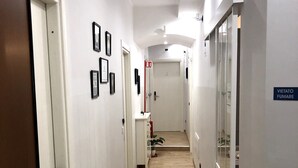 A hallway with a wooden floor, white walls, and doors on both sides. There are framed pictures on the walls and a sign that reads "Vietato Fumare". - Avec Moi Roma (Rome)