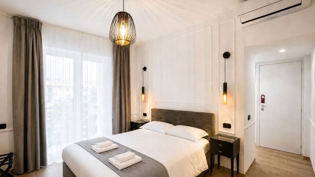 A hotel room with a large bed, bedside tables, a hanging light fixture, and a door with a lock. - Avec Moi Roma (Rome)