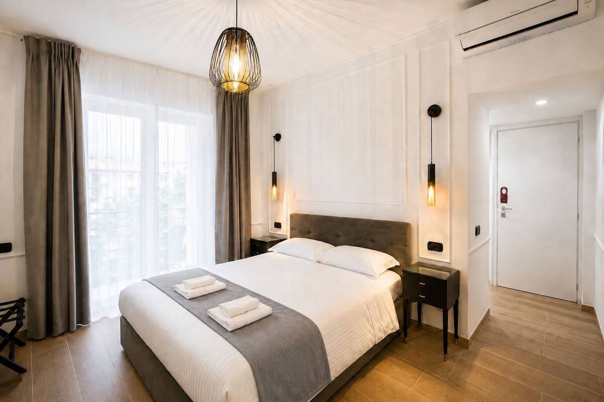 A hotel room with a large bed, bedside tables, a hanging light fixture, and a door with a lock.