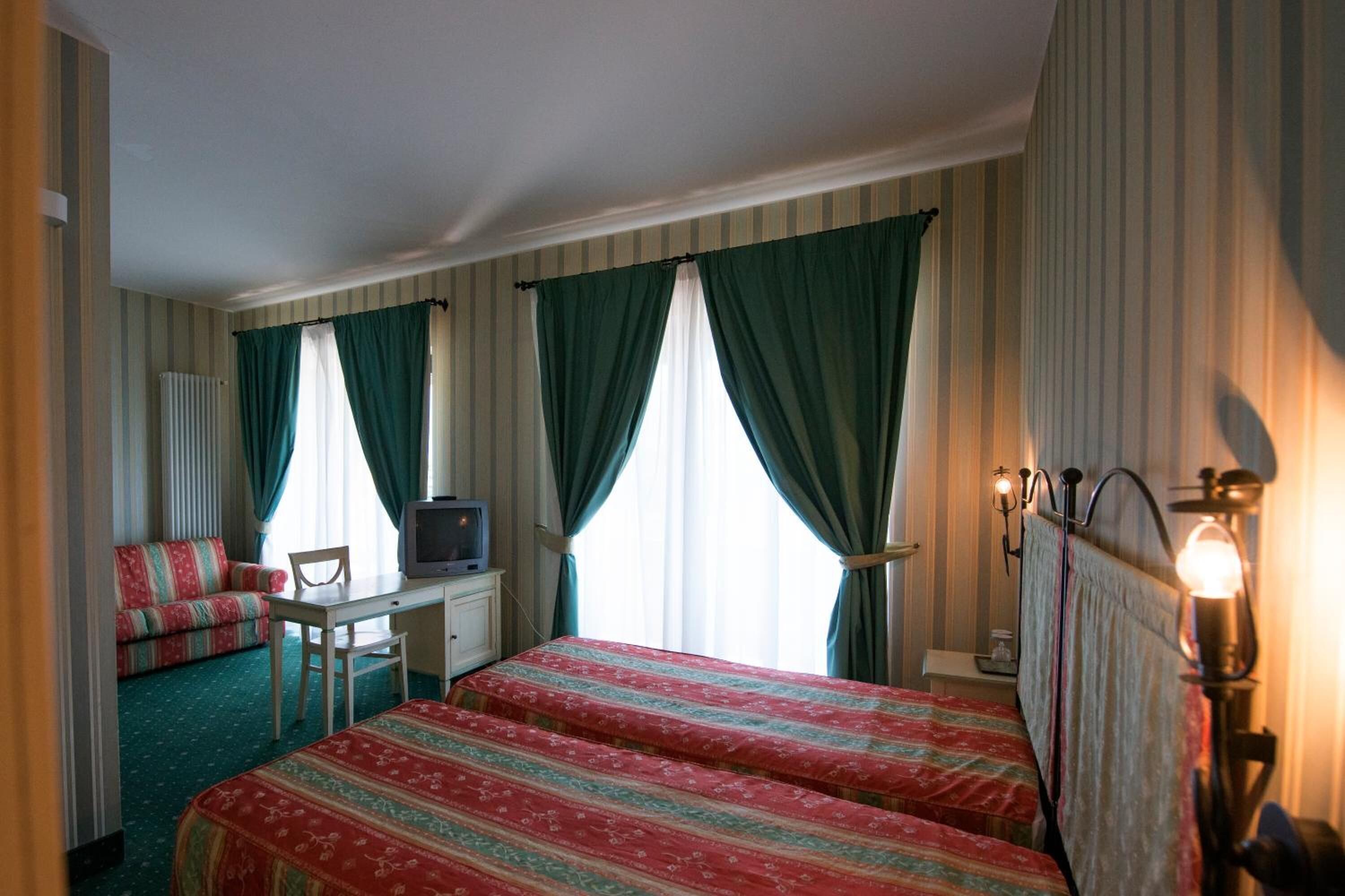 Una habitación de hotel con dos camas, un escritorio con televisor, un sofá y una lámpara.