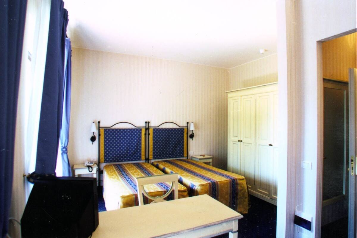 A hotel room with a bed, a desk, a chair, and a wardrobe.
