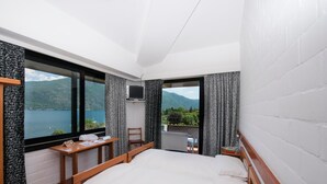 Habitación de hotel con una cama grande, un escritorio, una silla, un televisor y vistas a un lago y montañas.