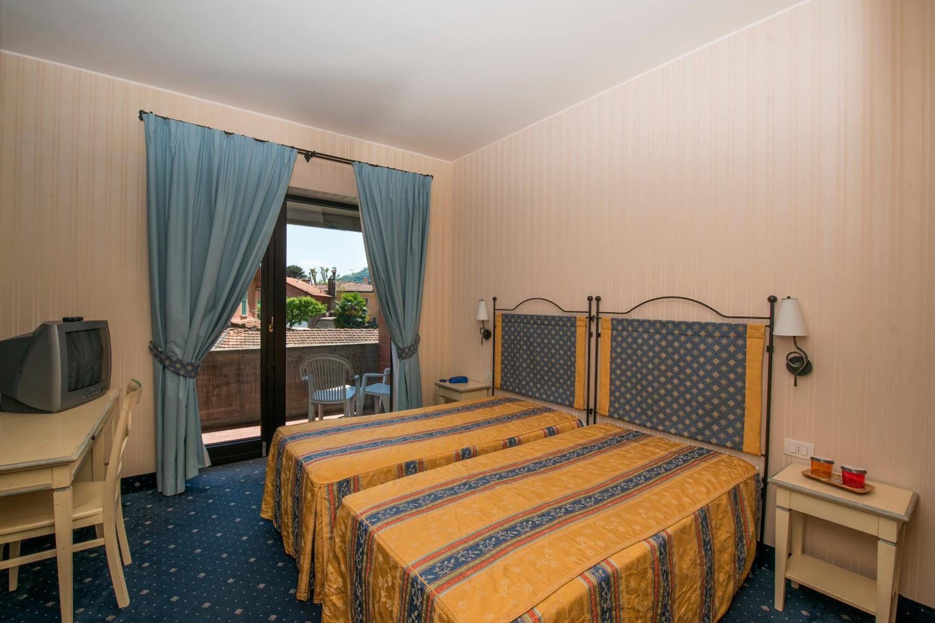 Hotellihuone, jossa on sänky, työpöytä, jossa on televisio, pieni pöytä ja ikkuna, jossa on verhot.