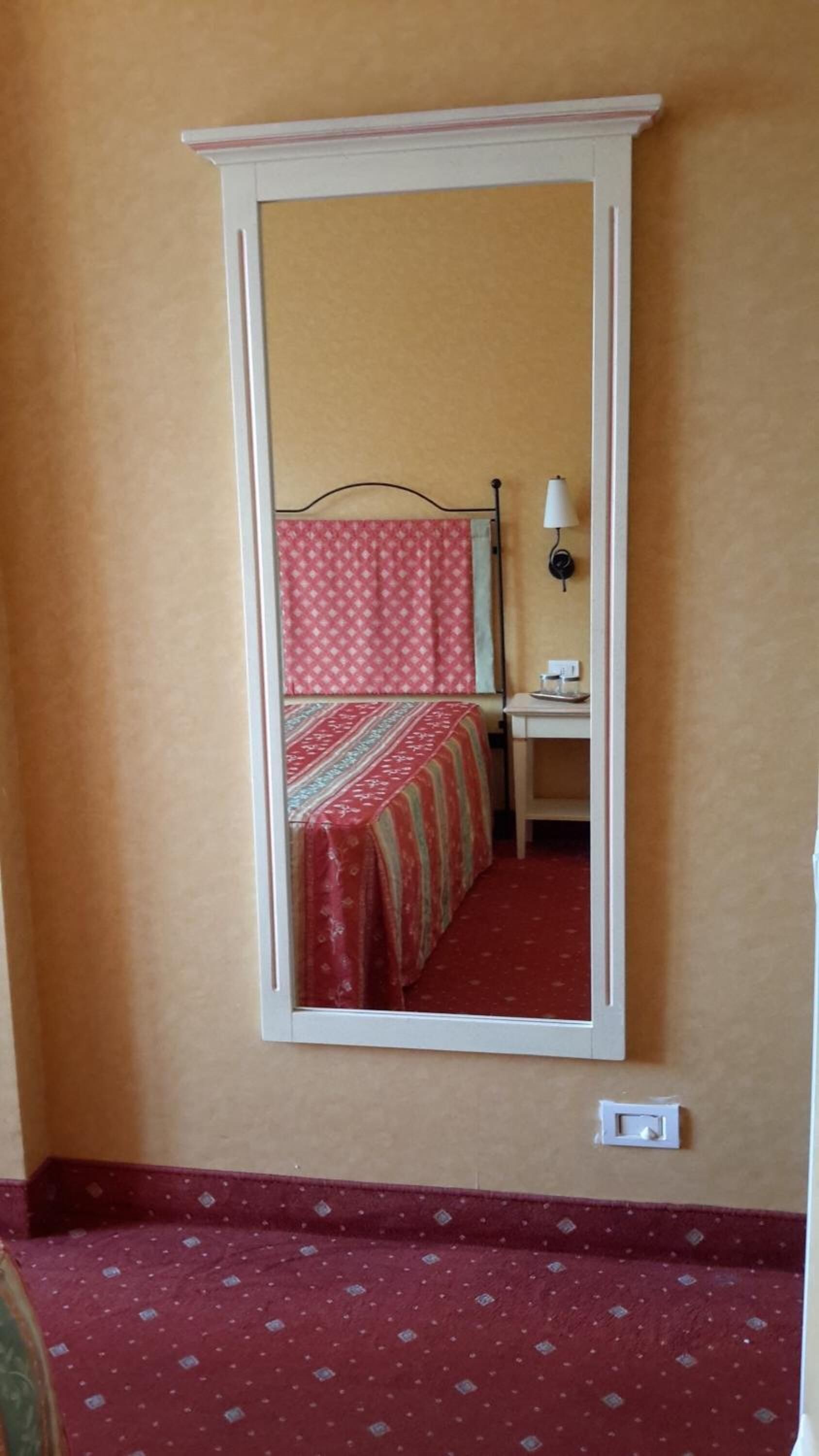 A room with a bed, a desk, and a mirror on the wall.
