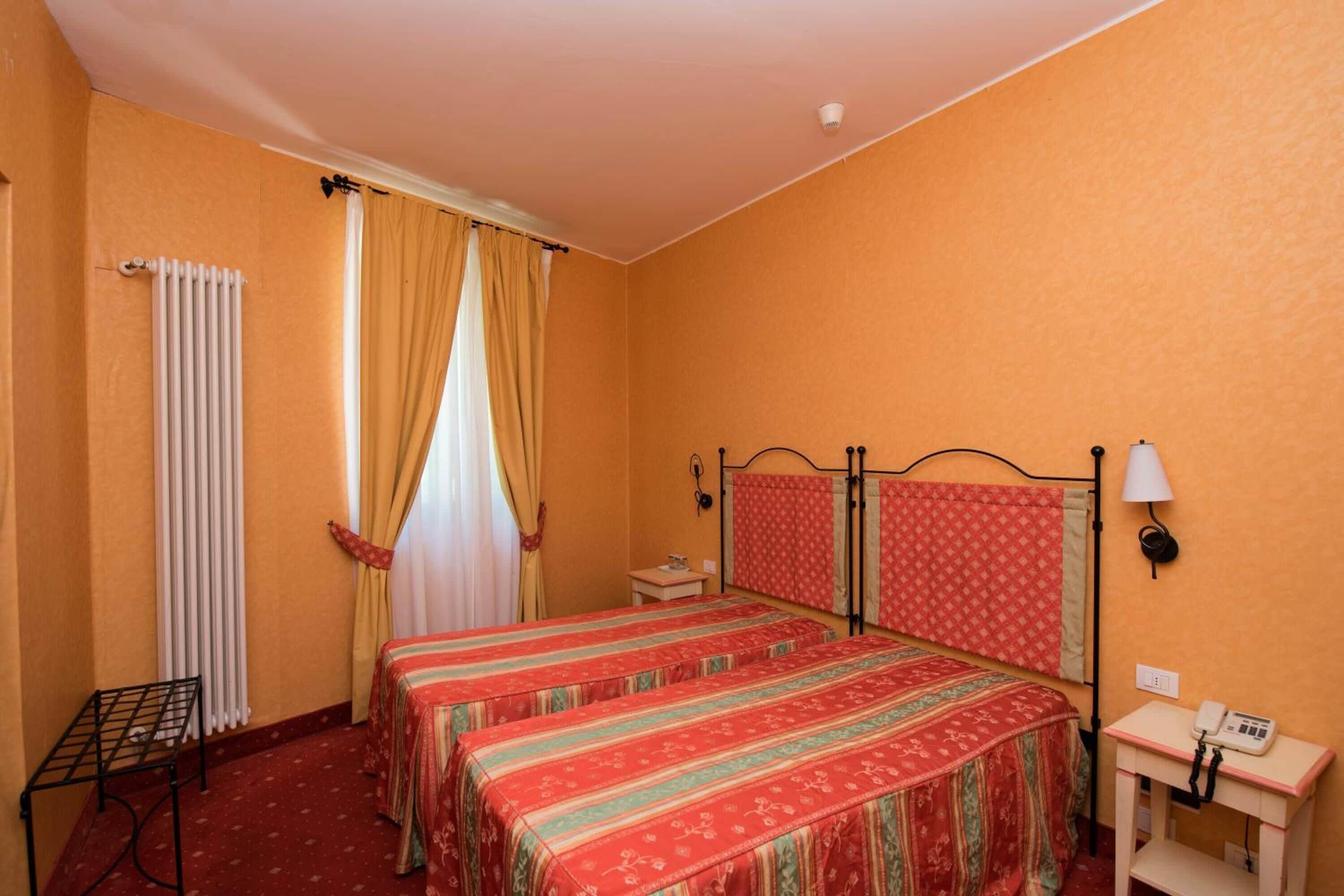 Une chambre avec deux lits, un radiateur, une petite table, une lampe et un téléphone.
