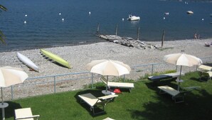 Una zona de playa con sillas de descanso y sombrillas, un litoral rocoso y barcos en el agua.