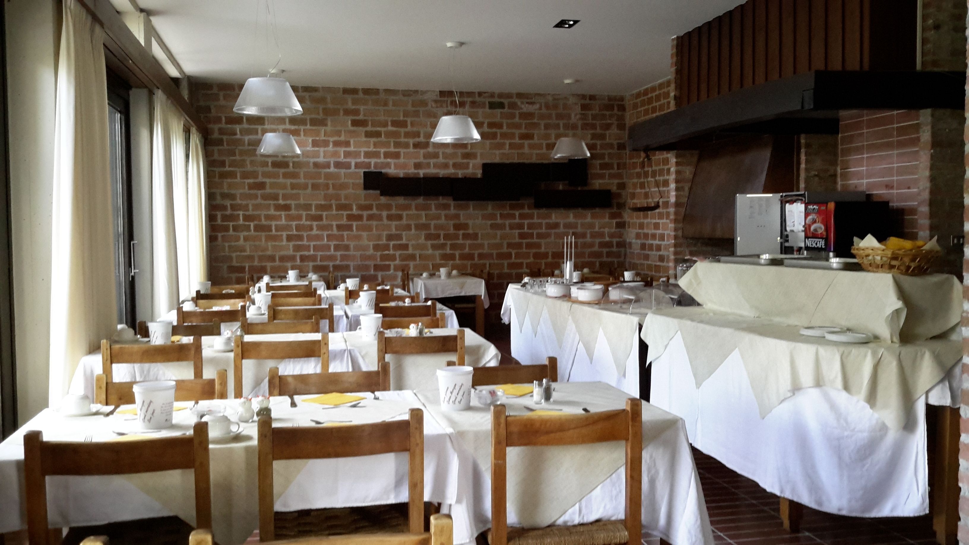 Un espace repas avec des murs en briques, des tables blanches et des chaises en bois.