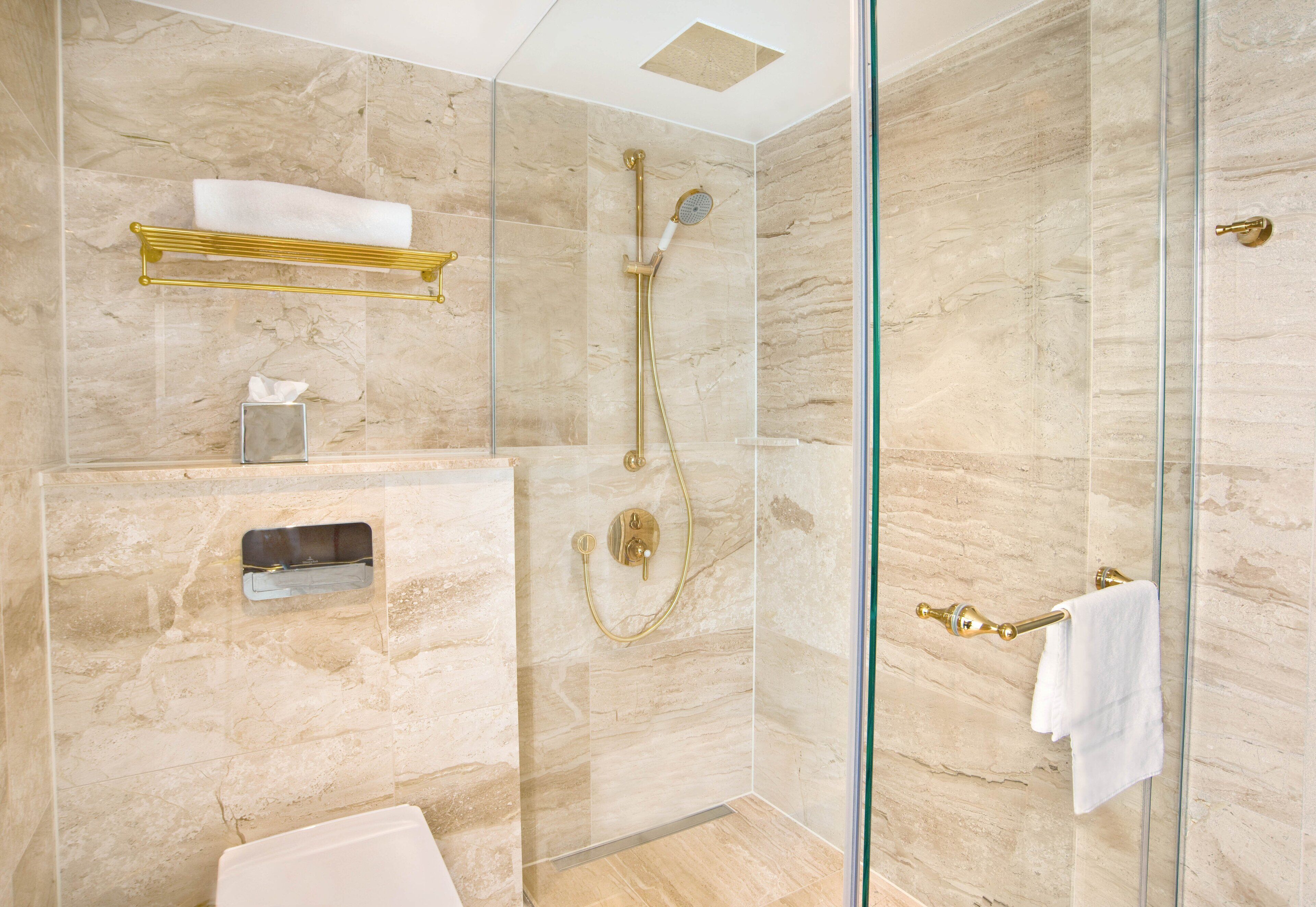 Un baño moderno con cabina de ducha de vidrio, paredes de mármol, un perchero dorado y un inodoro.