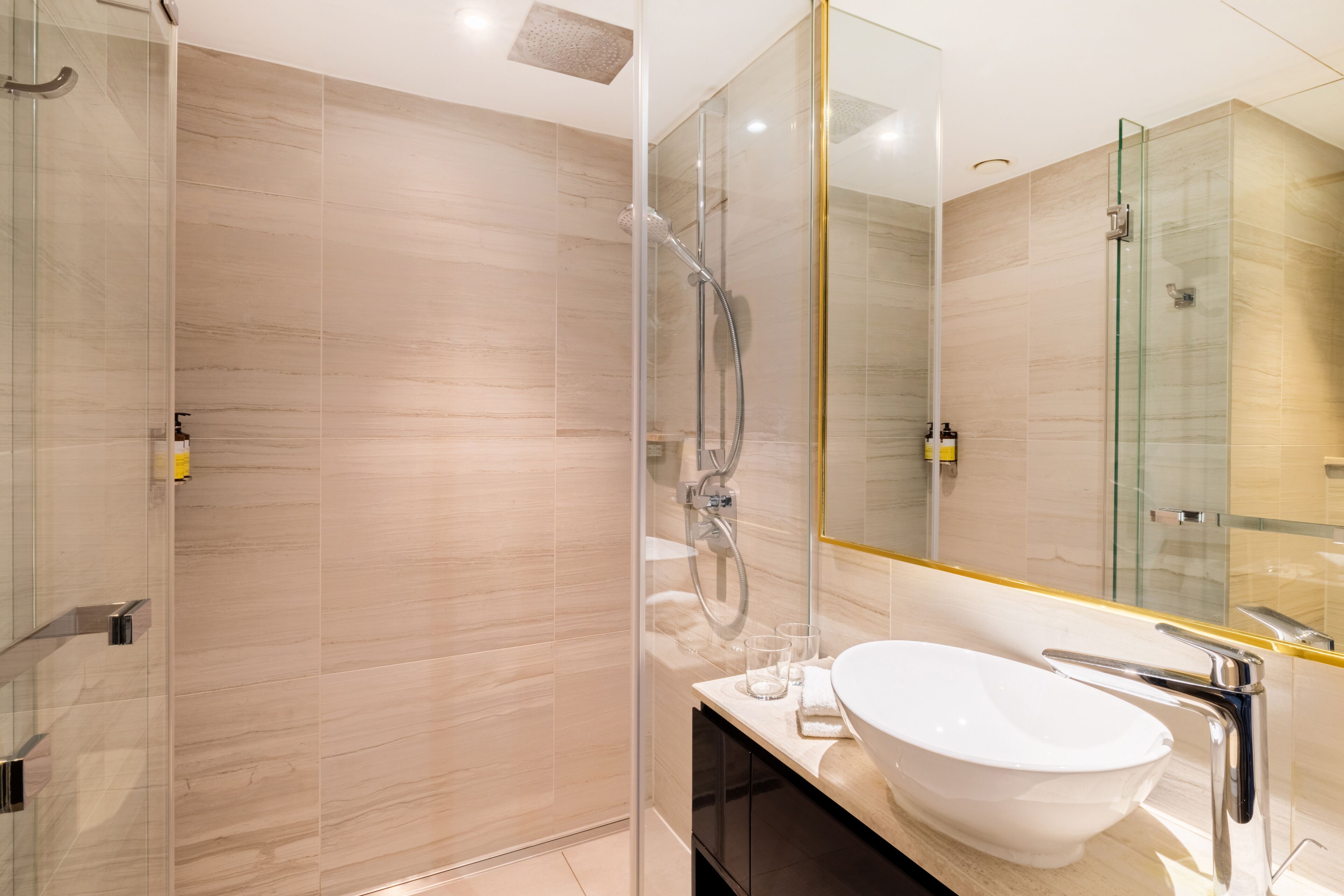 A modern bathroom with a glass-enclosed shower, a white sink, and a large mirror.