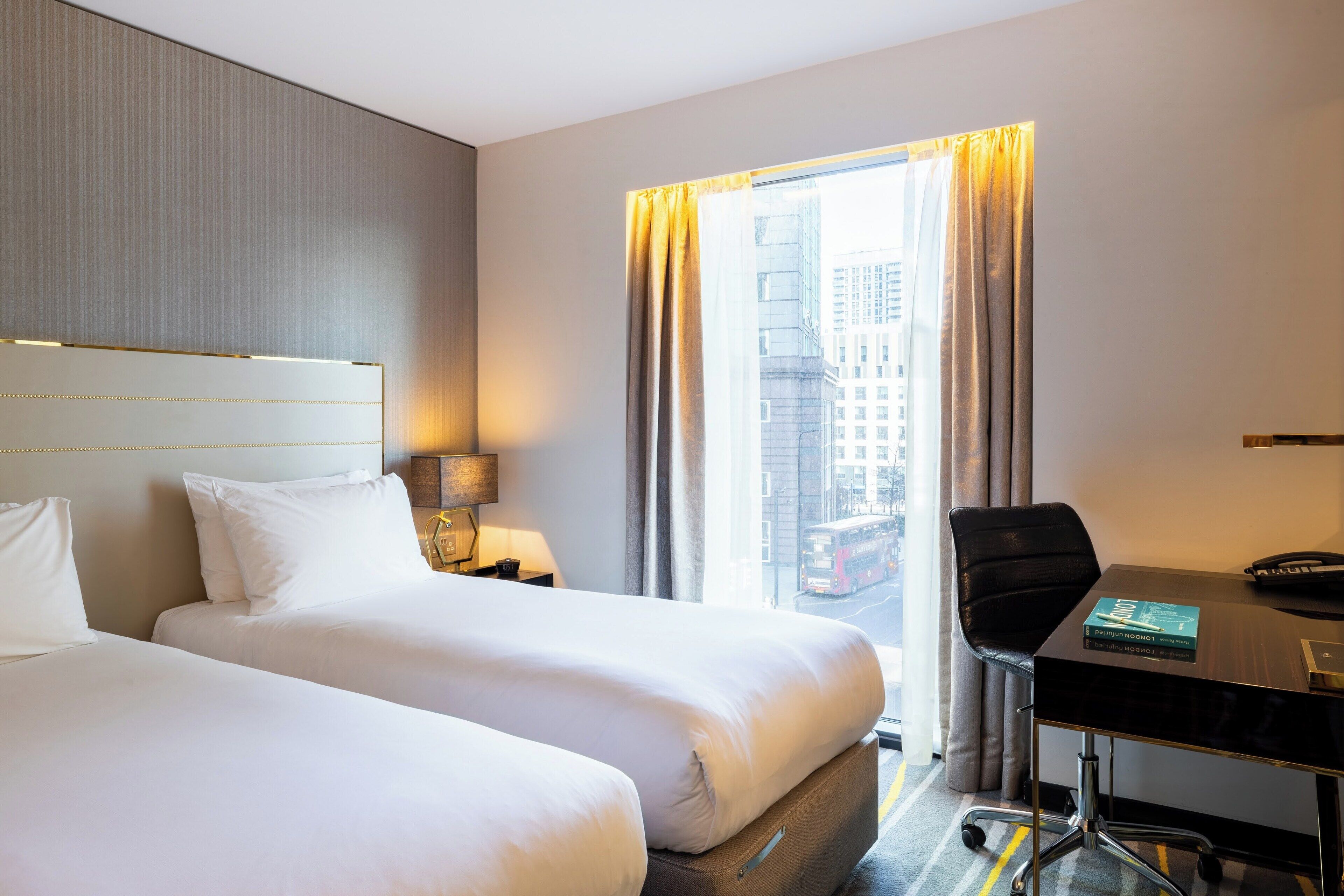 Une chambre d’hôtel avec deux lits, un bureau, une chaise, une lampe et une vue sur la ville.