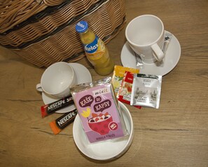 Una escena de desayuno con una cesta de mimbre, una botella de jugo de naranja, dos tazas blancas, un plato con un sobre de mezcla y dos sobres de crema para café Nescafé Classic.