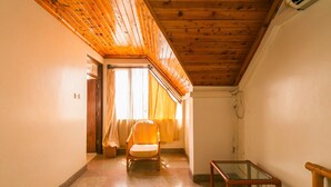 Um corredor com teto de madeira, uma cadeira, uma mesa de vidro e uma porta que dá para outro quarto.