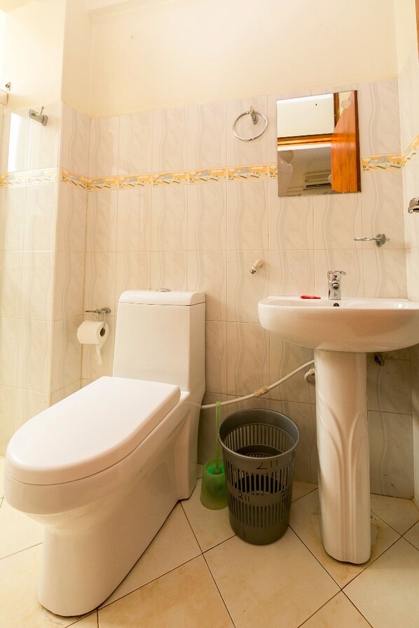Un baño con inodoro, lavamanos y un cubo de basura.