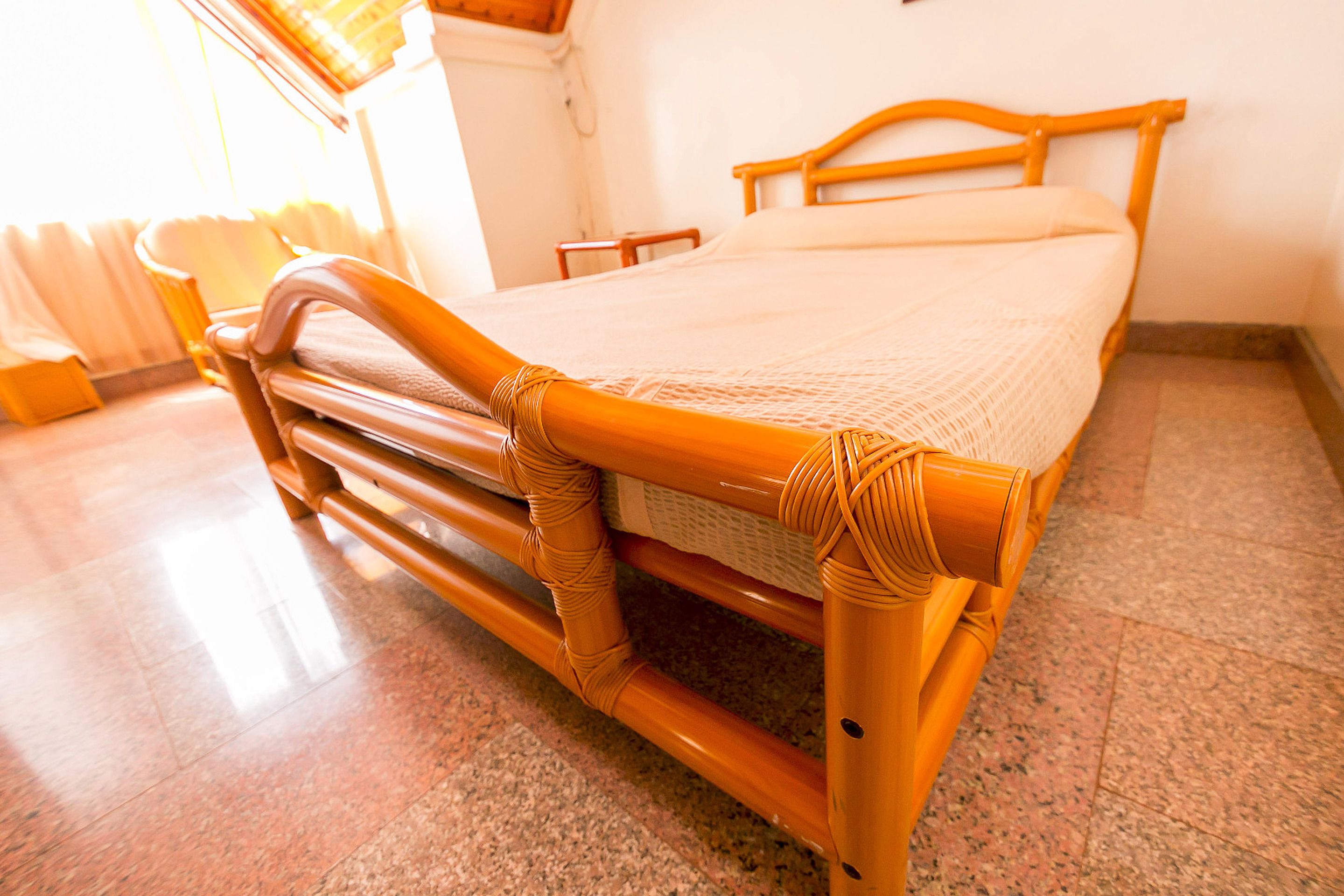 A bed with a wooden frame and a woven headboard, a bedside table, and a window with curtains.