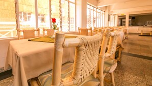 Um restaurante com cadeiras de vime, mesas e grandes janelas.