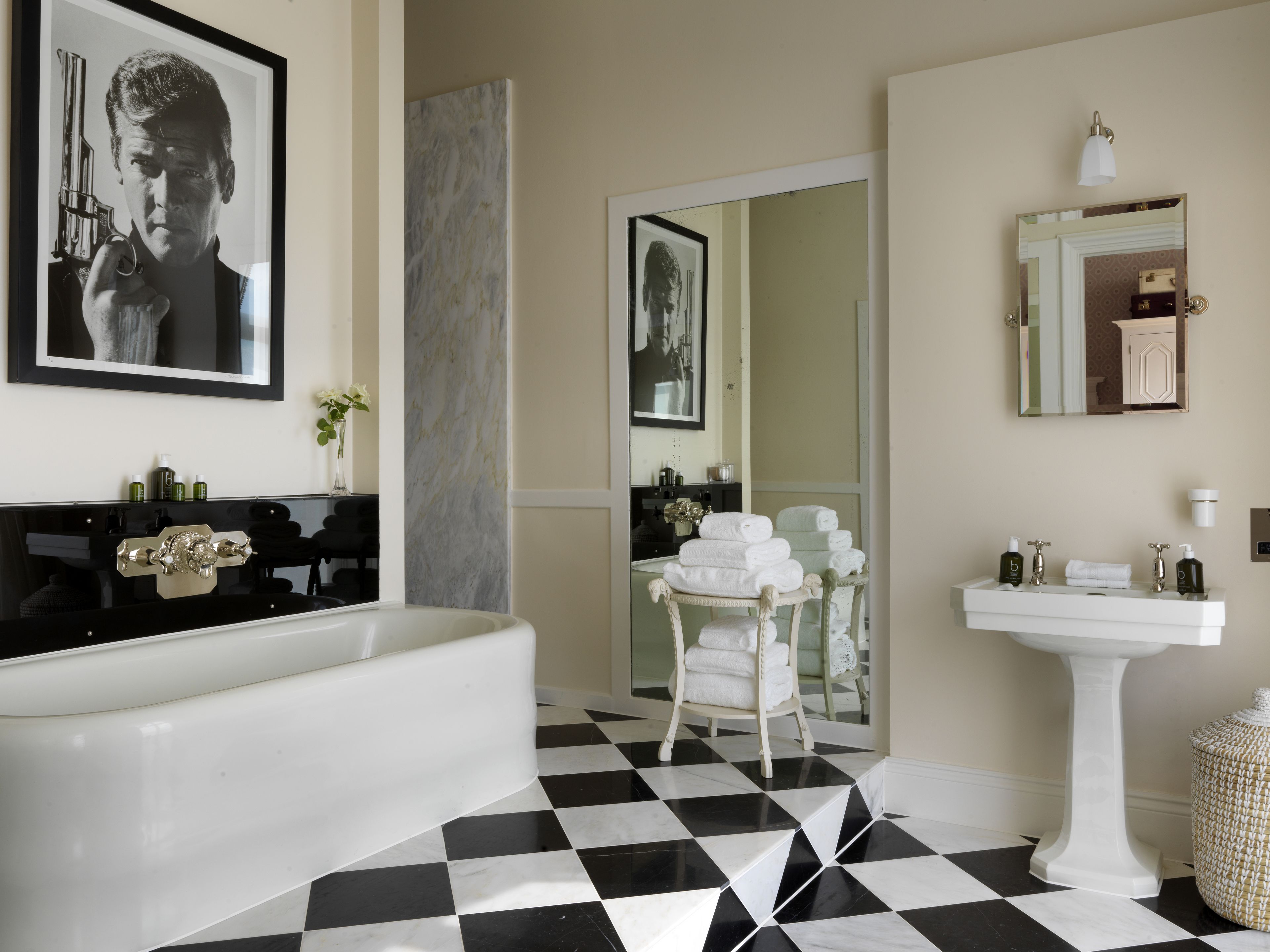Un baño con piso a cuadros blanco y negro, una bañera blanca, un lavamanos blanco y un espejo sobre el lavamanos.