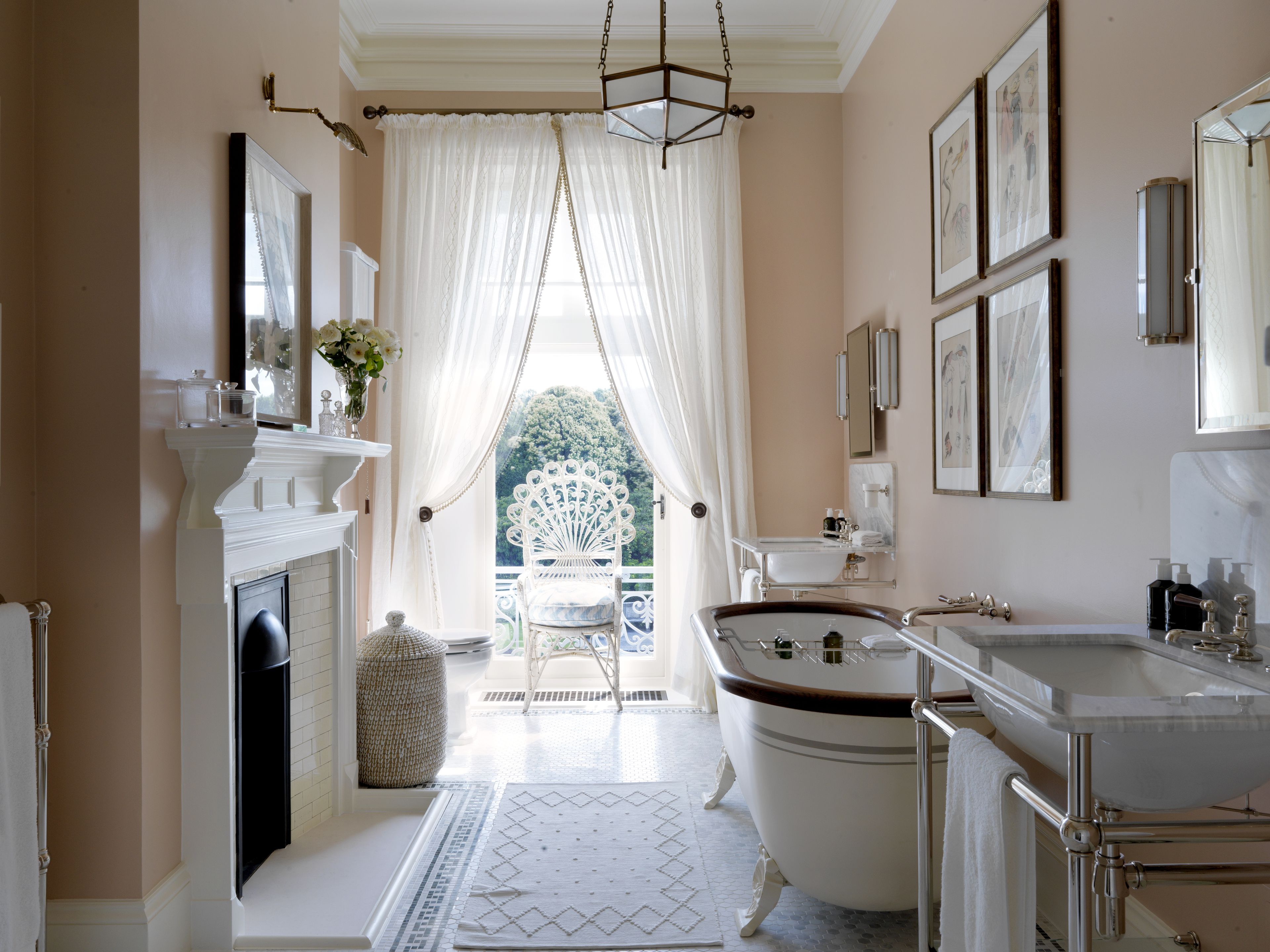 Un baño con bañera, lavabo y espejo. Se ve una ventana con cortinas y vistas al exterior con vegetación.