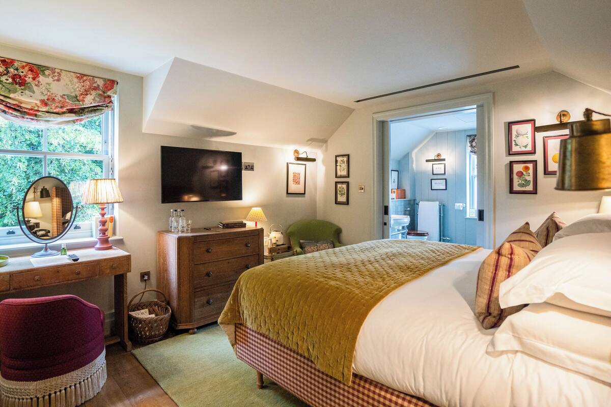 A bedroom with a bed, a dresser, a mirror, a television, and a window with curtains.