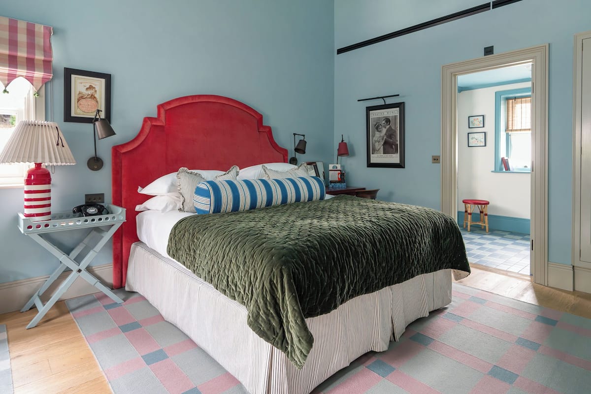 A bedroom with a red headboard, a striped pillow, and a green blanket.