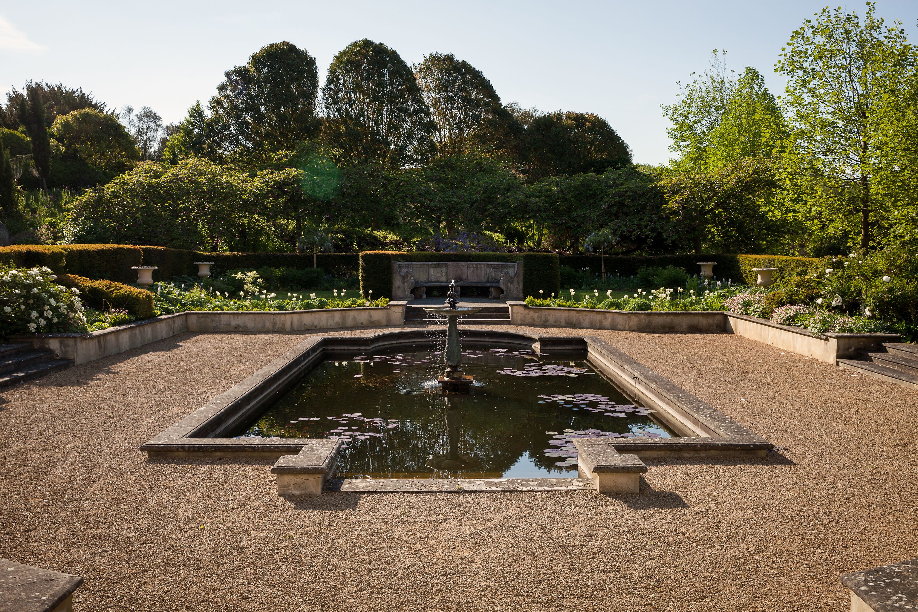A garden with a central fountain, surrounded by neatly trimmed hedges and flowering plants.