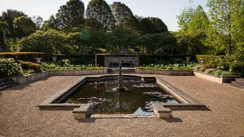 A garden with a central fountain, surrounded by neatly trimmed hedges and flowering plants.