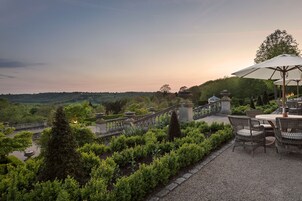 Un patio jardín con mesa y sillas, rodeado de setos cuidados y vistas al paisaje.