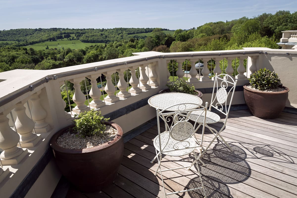 A wooden deck with a white metal table and chairs, surrounded by potted plants.