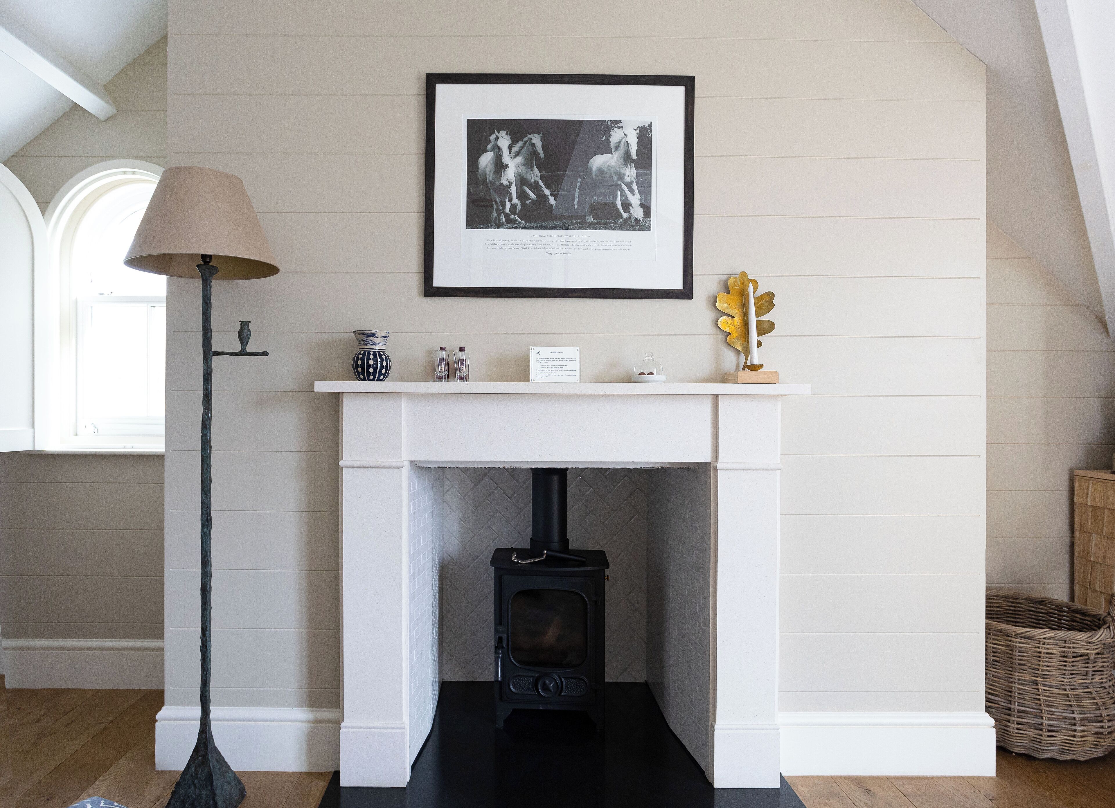 A room with a white fireplace, a framed picture above it, and a lamp to the left.