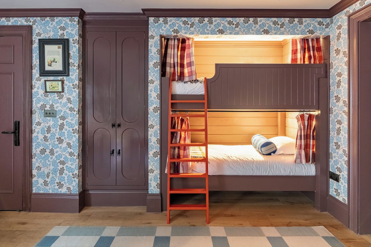 A room with a bunk bed, wooden wardrobe, and patterned wallpaper.