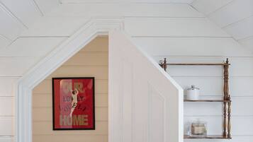 A hallway with a white door, a chandelier, a framed sign on the wall, and a shelf with a container.