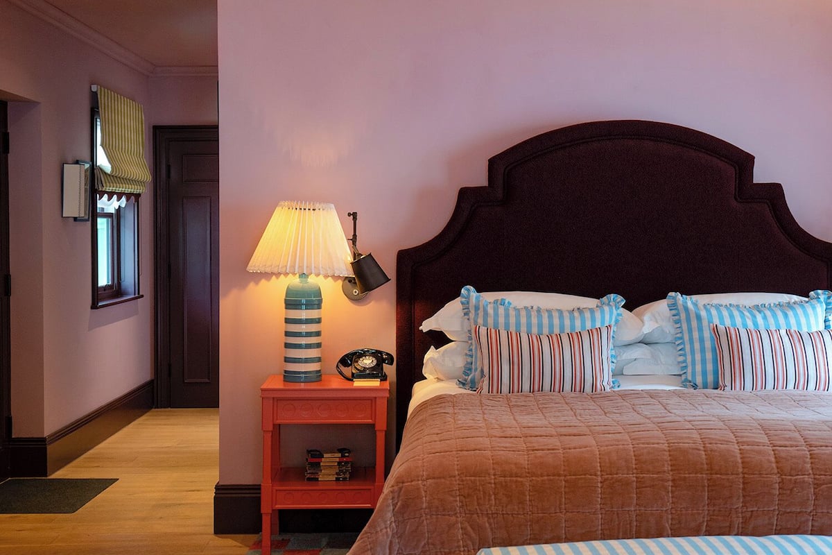 A bedroom with a bed, bedside table, lamp, and a checkered rug.