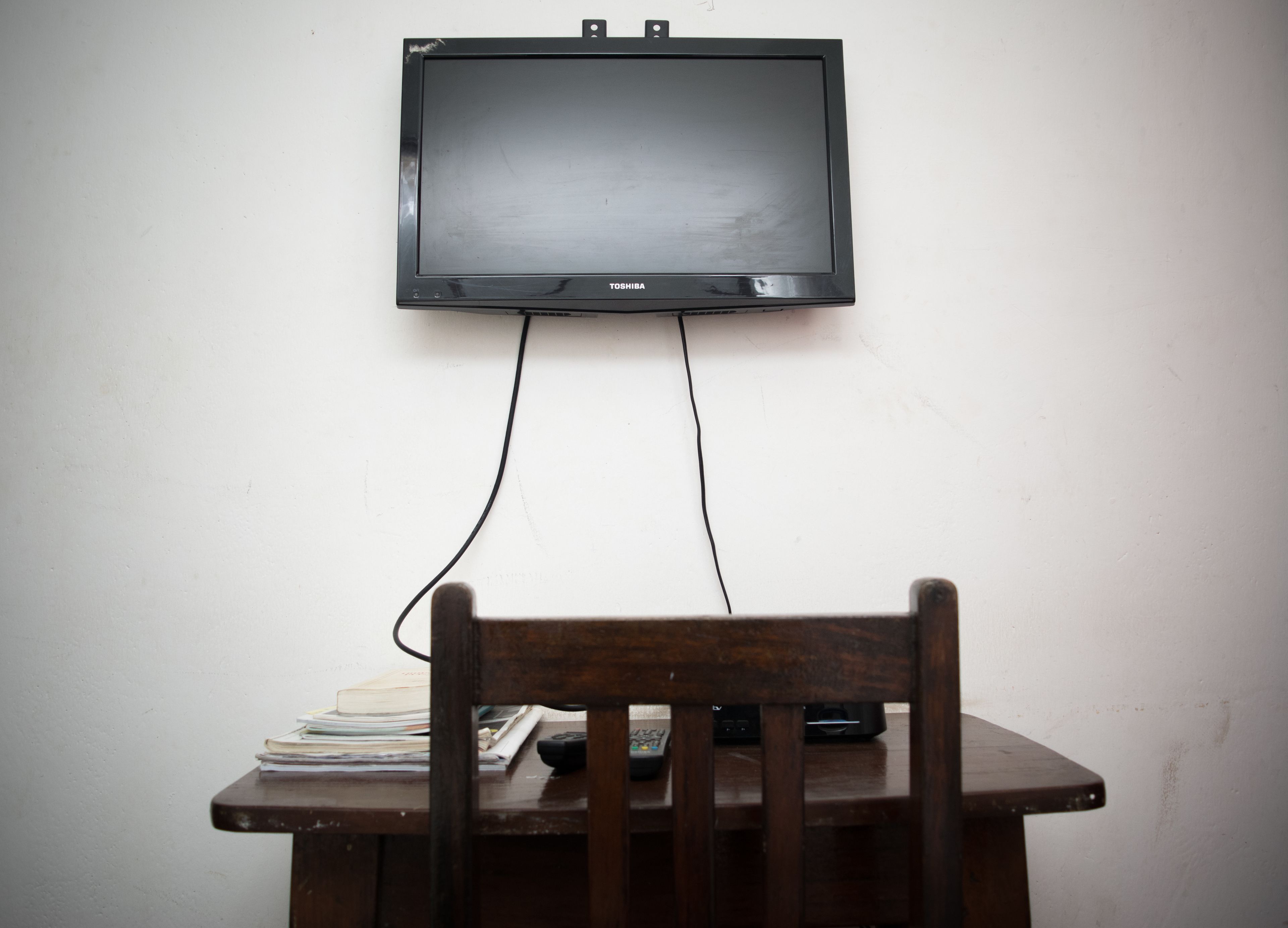 Un téléviseur fixé au mur, au-dessus d’une table en bois, avec une chaise placée devant.