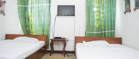 Una habitación con dos camas de madera, una mesita con televisor y cortinas verdes.
