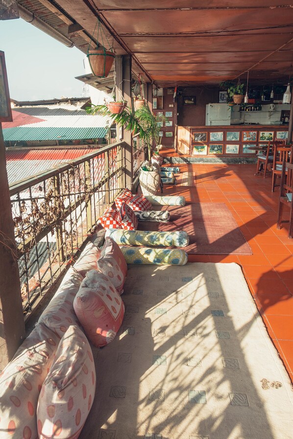 A covered outdoor seating area with cushioned benches and a variety of potted plants.