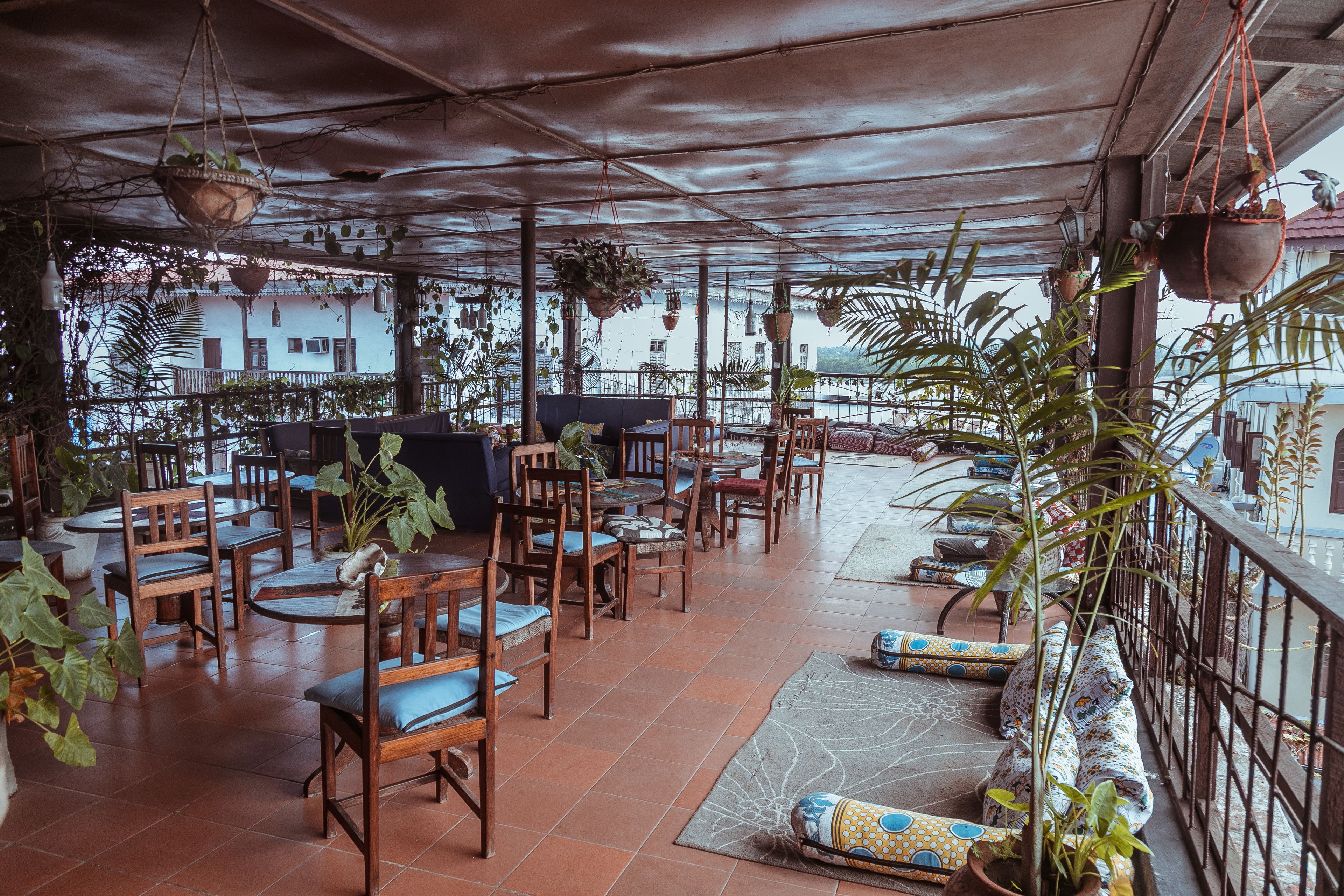 An outdoor seating area with wooden tables and chairs, surrounded by potted plants and hanging planters.
