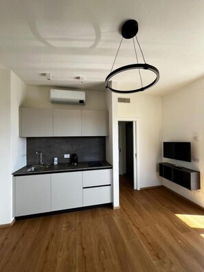 Una cuina moderna amb armaris blancs, taulell negre i llum penjant.