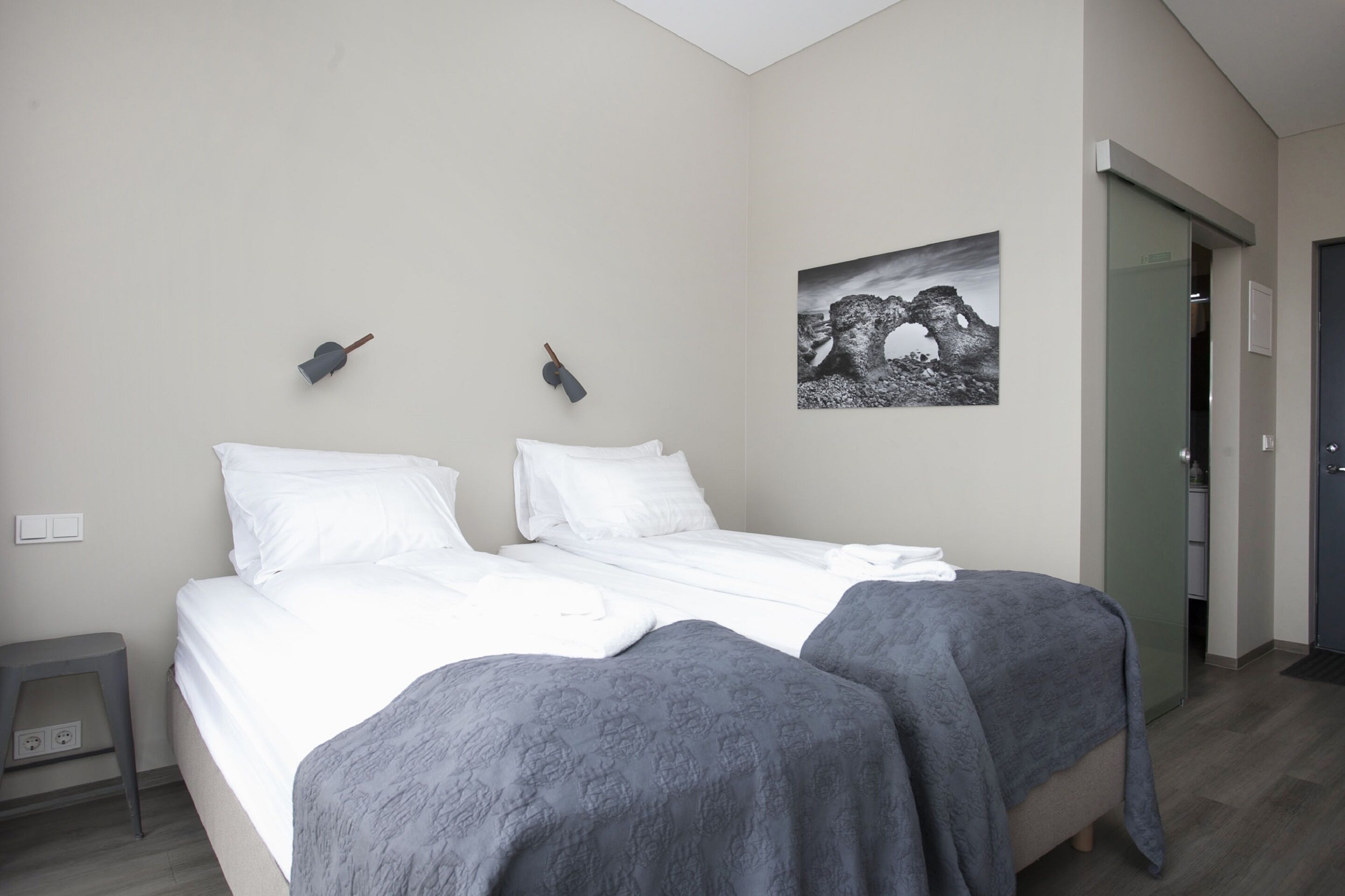 A bedroom with a bed, two bedside tables, a wall-mounted lamp, and a framed picture.