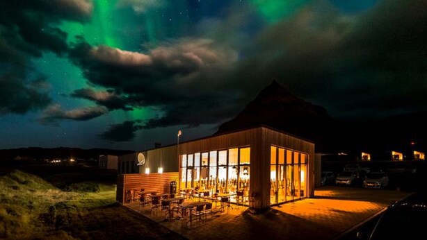 En byggnad med en bar och stora fönster, under en stjärnklar natthimmel där norrskenet syns tydligt.