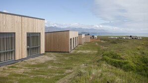 En rad moderna trähus med stora fönster, en gräsyta framför och berg i bakgrunden.