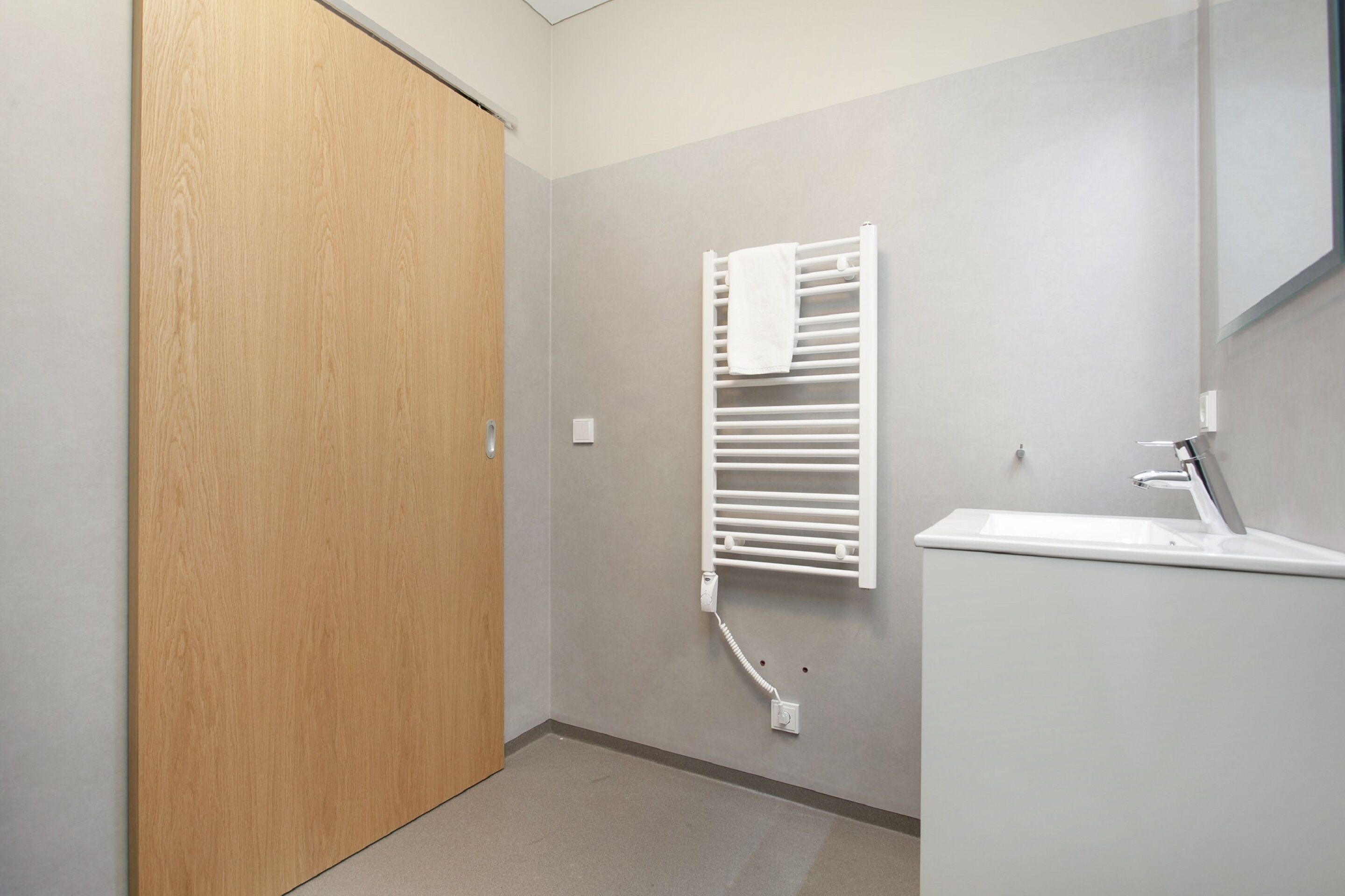 A bathroom with a wooden door, a towel rack, a sink, and a mirror.