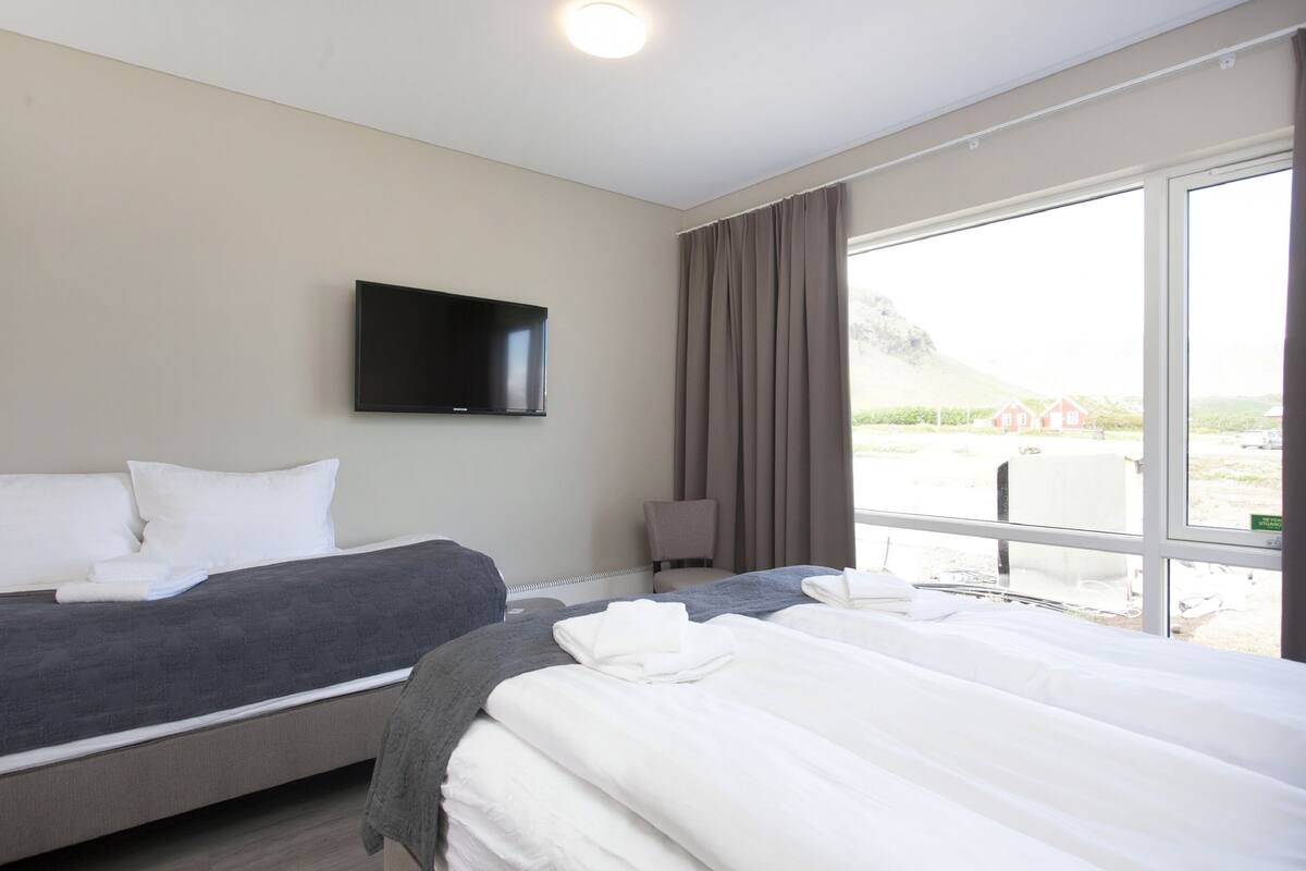 Une chambre d’hôtel avec deux lits, un téléviseur à écran plat fixé au mur et une grande fenêtre donnant sur l’extérieur.